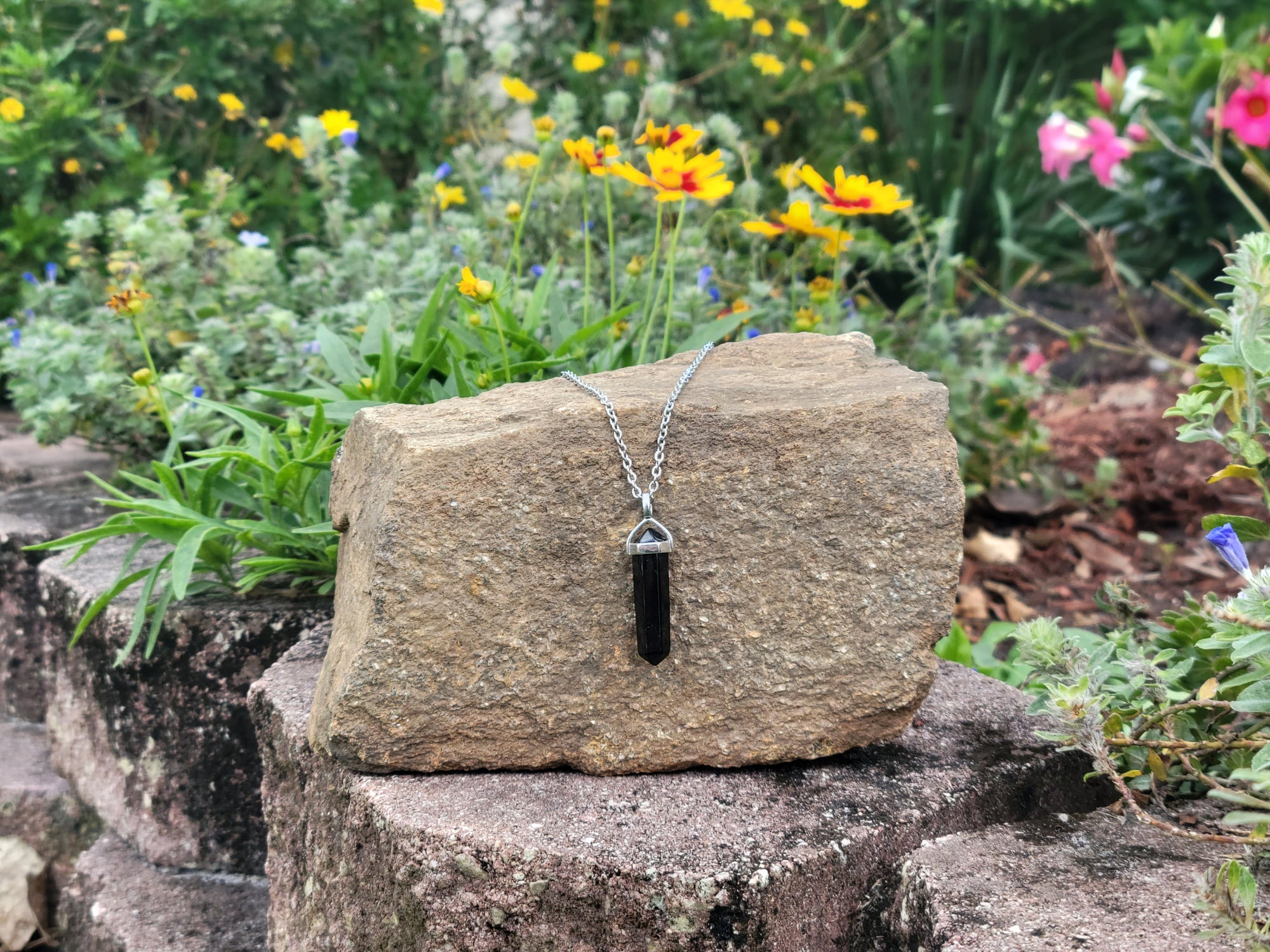 Unisex 6-Point Hexagonal Shungite Pendant Necklace on a stainless steel chain, resting on a large rock