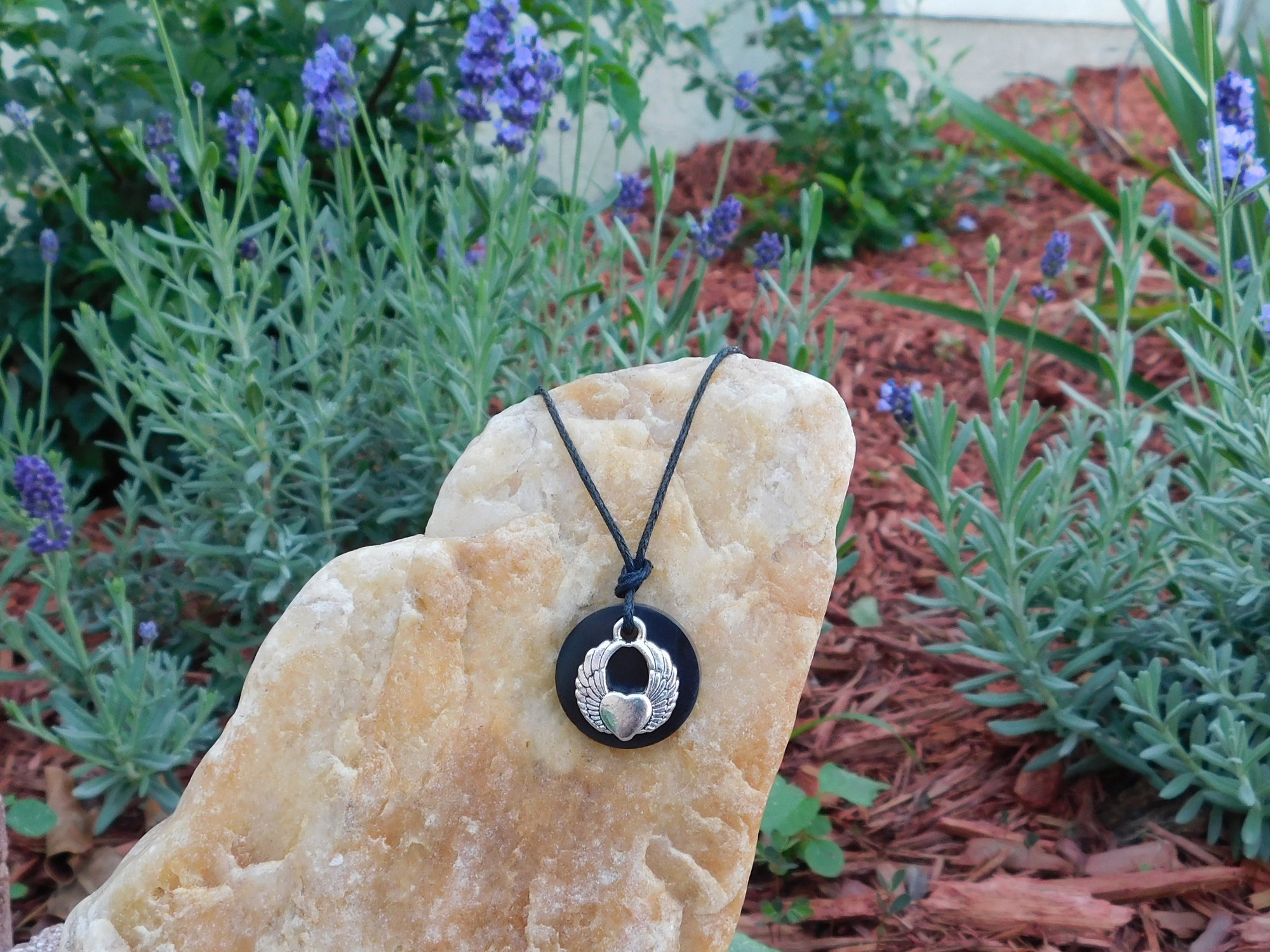 Angel Wing Shungite Pendant Necklace with an adjustable cotton cord, resting on a rock