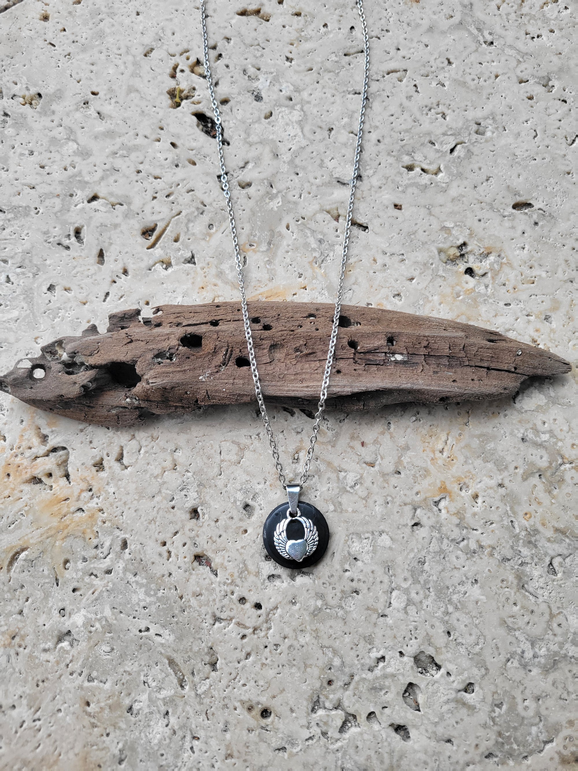 Shungite disk pendant with a small angel wing charm on a long stainless steel chain